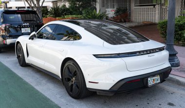 Miami Beach, Florida USA - 9 Haziran 2024 Miami plajında Porsche Taycan beyaz rengi. Ocean 'daki lüks araba porshche' si Miami plajına gidiyor. ön köşe görünümü