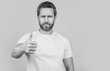 Ciddi adam stüdyoyu, seçici odak noktasını ve kopyalama alanını onaylıyor. Onaylanmış bir adamın fotoğrafı. Baş parmağıyla. Sarıda izole edilmiş bir adam. adam arka planda onaylar.