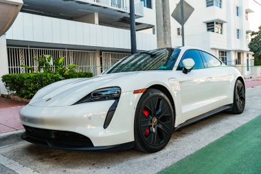 Miami Beach, Florida USA - 9 Haziran 2024 Miami plajında Porsche Taycan beyaz rengi. Ocean 'daki lüks araba porshche' si Miami plajına gidiyor. ön köşe görünümü