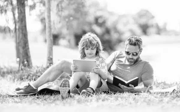 stock image Father and son child relax in park. childhood school education. son with father bonding. family education of father and son kid. Father shapes son education with book tablet. connecting with nature.