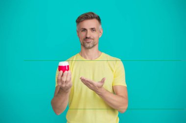 Olgun bir adam mavi üzerine izole edilmiş kremin cilt ürününü sunar..