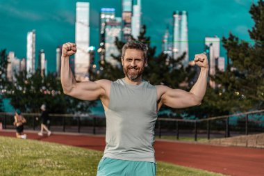 Sporcu pazılarını ve pazılarını göster. Adam pazılarıyla kollarını esnetiyor. Güçlü kaslı sporcu. Dışarıda spor antrenmanı. Antrenmandan sonra sporcu. Spor yapan adam. Pazı kavramı. Vücut geliştirici.