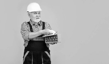 Sarı arka planda kasklı yaşlı adam gülümsüyor..
