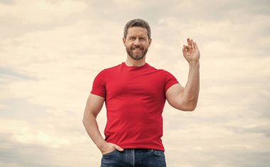 happy man in red shirt outdoor on sky background. ok. clipart