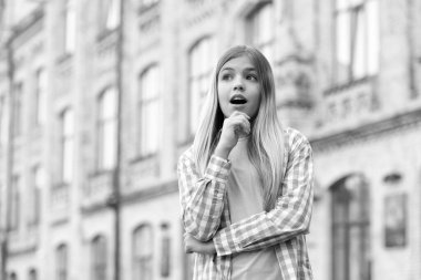 Surprised teen girl looking away with chin on hand blurry outdoors, copy space.