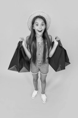 full length of amazed teen child with shopping bags on yellow background.