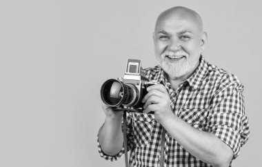 happy mature man with retro photo camera on yellow baqckground.