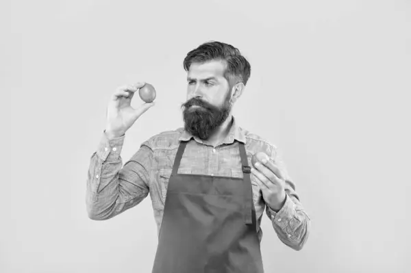 stock image Serious man in apron looking at fresh limes citrus fruits yellow background, greengrocer.