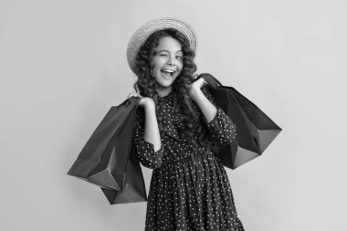 Kıvırcık saçlı, göz kırpan kız sarı arka planda alışveriş torbaları tutuyor..