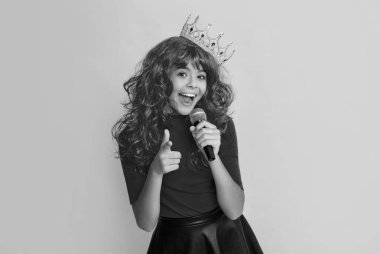 happy kid in crown with microphone on yellow background.