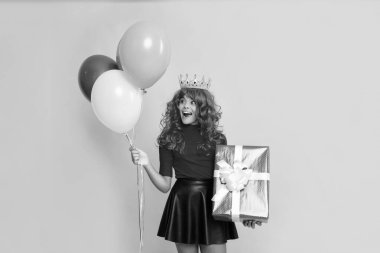 Sarı arka planda mevcut kutuyla ve parti balonuyla taç giymiş şok olmuş bir çocuk..