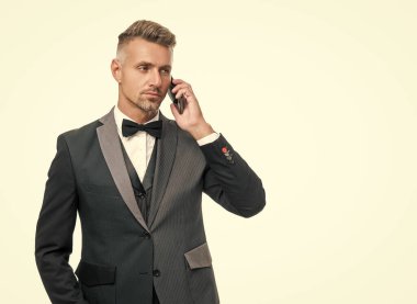 Smokinli iş adamı, beyaz arka planda izole edilmiş akıllı telefondan konuşuyor..