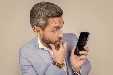 Ürün teklifi. Reklam sunumu, kopyalama alanı. Olgun adam telefon ekranını sunuyor. İş adamı gri alanda izole akıllı telefon gösteriyor. Takım elbiseli harika adam yeni bir uygulama önerdi..