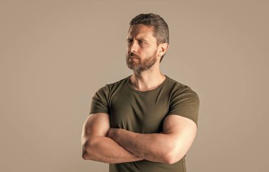 Stüdyoda kendine güvenen kaslı adam. Sakallı kaslı adamın fotoğrafı. Kaslı adam tişört giyer. Gri arka planda sakallı, kaslı bir adam..