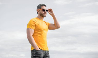 Gökyüzü arka planında sarı gömlekli ve güneş gözlüklü bir adam. yaz modası.