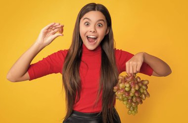 surprised girl hold fresh grapes fruit on yellow background.