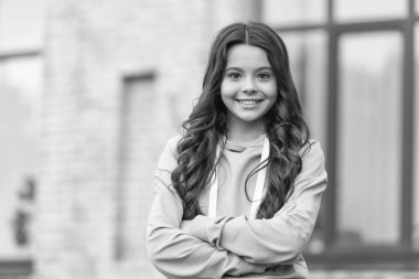 Confident teen girl happy smiling in casual hoodie keeping arms crossed blurry outdoors.