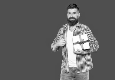 Gri arka planda hediye kutusu olan olgun sakallı adam. özel selamlama.