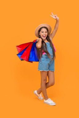 happy teen girl with shopping bags show peace on yellow background. full length.