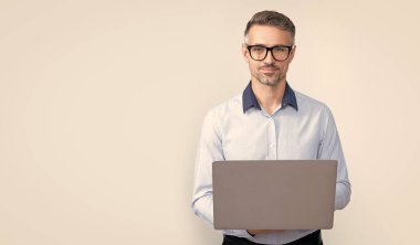 Gri arka planda bilgisayar üzerinde çalışan gözlüklü olgun bir serbest yazar..