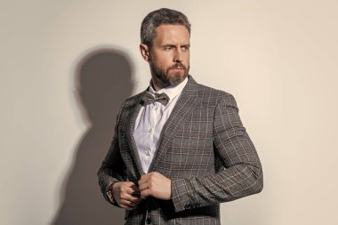 Stüdyodaki traşsız smokinli adam. Smokin giyen adamın fotoğrafı. Adam smokin resmi takım elbise giyiyor. Gri arka planda smokinli adam..