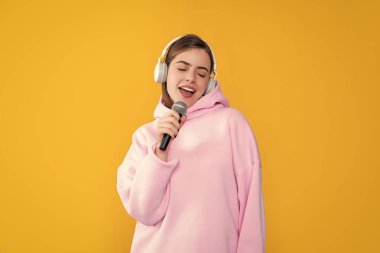 Sarı arka planda mikrofonu olan kulaklıklı genç kız..