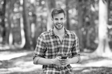 young handsome man in checkered shirt blogging on phone outdoor.