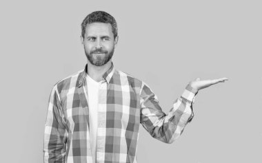 photo of caucasian guy wear checkered shirt presenting copy space. caucasian guy wearing casual style. bearded caucasian guy in casual shirt isolated on yellow background. caucasian casual guy