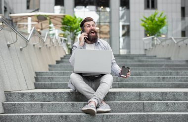 Dışarıda serbest iletişimi olan gülen adam. Açık havada serbest iletişimde olan bir adam. Serbest çalışan bir adam telefonda konuşuyor. Dizüstü bilgisayarında serbest iletişimi olan bir adam..