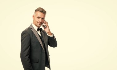 Smokinli neşeli adam beyaz arka planda izole bir şekilde telefonla konuşuyor..