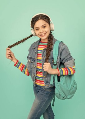 Kulaklıkla müzik dinleyen mutlu genç kız mavi arka plan, eğitim. Gayri resmi eğitim. Okul eğitimi.