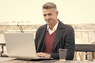 İnternette çalışan mutlu bir adam açık kafede kahve içiyor..