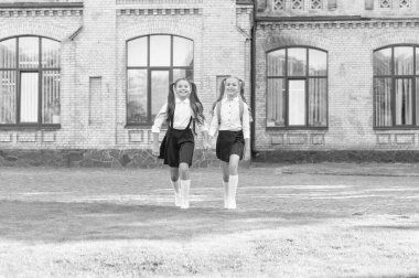 two teen girls in uniform walking together outdoor.