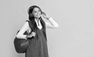 glad child in headphones with school backpack on yellow background.