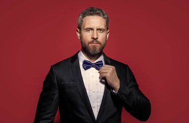 Stüdyoda resmi kıyafet. Formalite giymiş bir adamın portresi. Adam resmi smokin giyer. Formalite icabı smokinli adam kırmızı arka planda izole edilmiş..