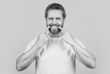 Mutlu adam sarı üzerine izole edilmiş diş tebessümünü gösteriyor. Adam arka planda gülümseyen dişlere işaret ediyor. Stüdyoda diş gösteren bir adam gülümsüyor. Adamın diş tebessümünü gösteren fotoğrafı..