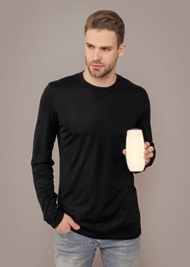 Stüdyoda tıraş losyonu kullanan genç bir adam. Erkek için tıraş losyonu. Yakışıklı adam elinde tıraş losyonu şişesi tutuyor. Adam tıraş losyonu ürününü gri arka planda tutuyor..