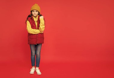 Kalın giysiler giyen bir çocuk. Duygularını ifade et. Kış modası. kopyalama alanı. Şapkalı, kıvırcık saçlı kızgın çocuk. Kadın manken. Yelek giyen genç kız..