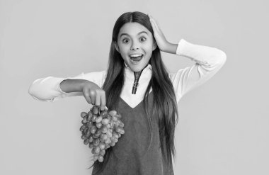 Şaşırmış çocuk sarı arka planda taze üzüm tutuyor. Vay..