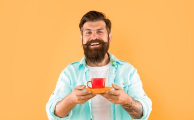 Sarı arka planda kahve fincanı tutan sakallı mutlu hippi..