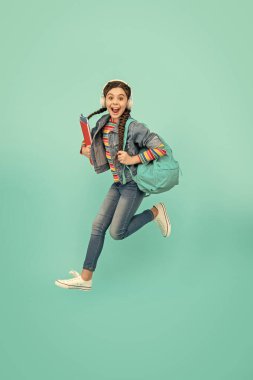 Heyecanlı liseli kız mavi arka planda atlıyor, eğitim görüyor. Enerjik genç kız havada çığlık atıyor. Okul eğitimi. Resmi olmayan ve gayri resmi eğitim.