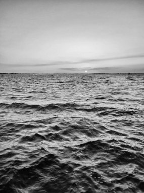 Gün batımında akşam gökyüzü altında deniz dalgaları olan bir su manzarası.