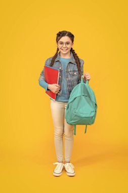 Happy teenage girl holding school bag yellow background. School education. Back to school.