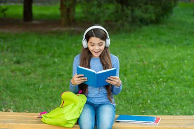 Okula dönelim. Eğitim ve bilgi. Şaşırmış kız sesli kitap dinleyip kitap okuyor. Audiobook kitaba karşı. Öğrenci kız. Okul eğitimi. Liseli kız kitap okur ve dışarıda sesli kitap dinler..