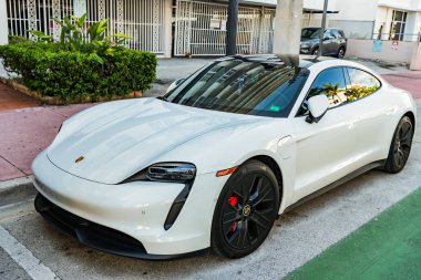 Miami Beach, Florida USA - 9 Haziran 2024 Miami plajında Porsche Taycan beyaz rengi. Ocean 'daki lüks araba porshche' si Miami plajına gidiyor. ön köşe görünümü