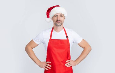 Kırmızı şef önlüğü ve Noel Baba şapkası giymiş neşeli olgun bir adam..