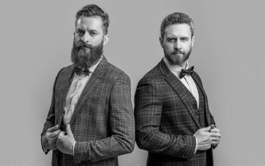 Resmi takım elbiseli şık erkekler. Gri arka planda karizmatik takım elbiseli adamlar izole edildi. Smokinli iki adam resmi kıyafet giyiyor. Stüdyoda resmi giyinen erkeklerin fotoğrafları..