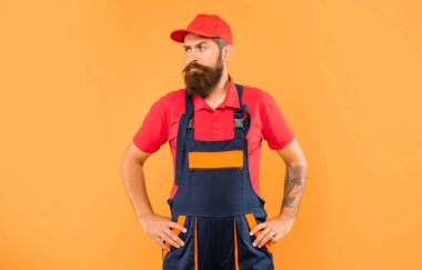 Sarı arka planda iş kıyafetleri içinde ciddi sakallı bir yükleyici..