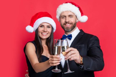 Şampanyayı seçen çift Xmas 'ı kutluyor. Xmas çifti kırmızı arka planda izole edilmiş şampanyayla kutluyor. Noel partisini şampanyayla kutlayalım. Stüdyodaki çifte mutlu xmas.