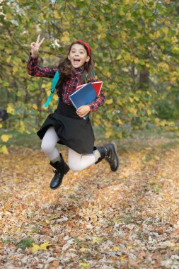 Sonbahar okulu ödevinde atlayan kız. Okula dönelim. Ödevi olan genç kız sonbahar parkında zıplıyor. Açık hava okulunda kız eğitimi. Bilgi ve eğitim. Sonbahar indirimi. Bilgi günü.